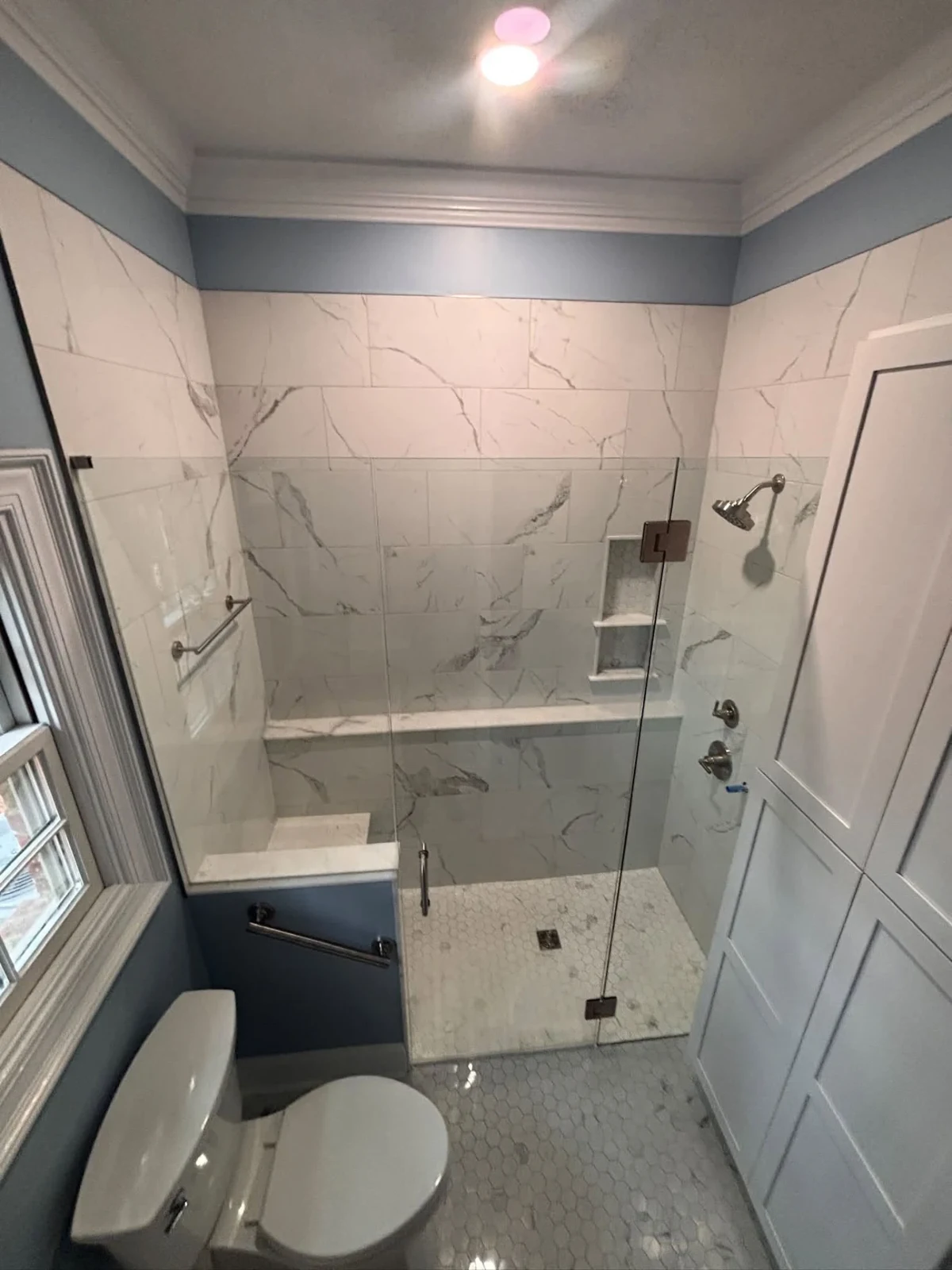 Marble-look tile, frameless glass and a custom shower bench.