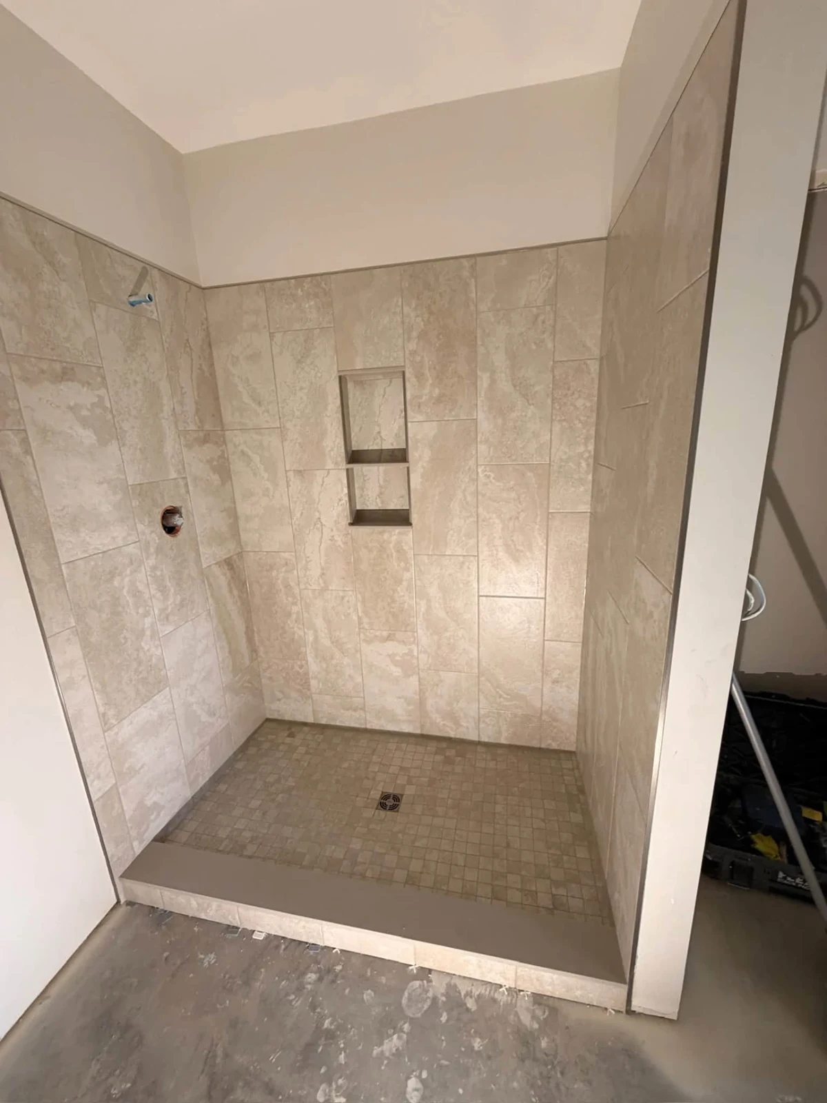 Natural-toned tile and a double recessed niche. Installation in progress.
