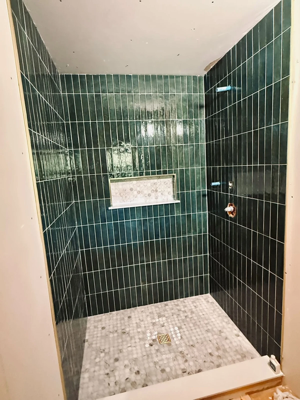 Deep green vertical tile and a recessed mosaic niche. Installation in progress.
